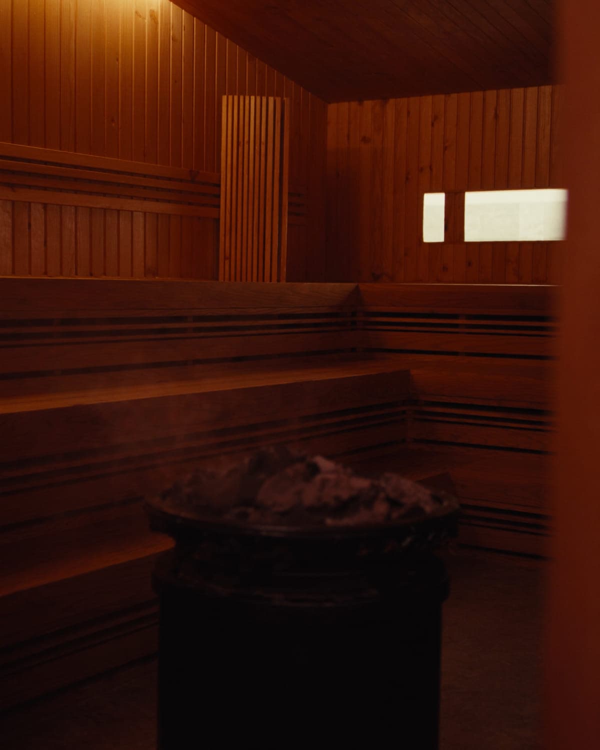Cedar-lined sauna with tiered benches and a stone-topped heater, lit low and warm